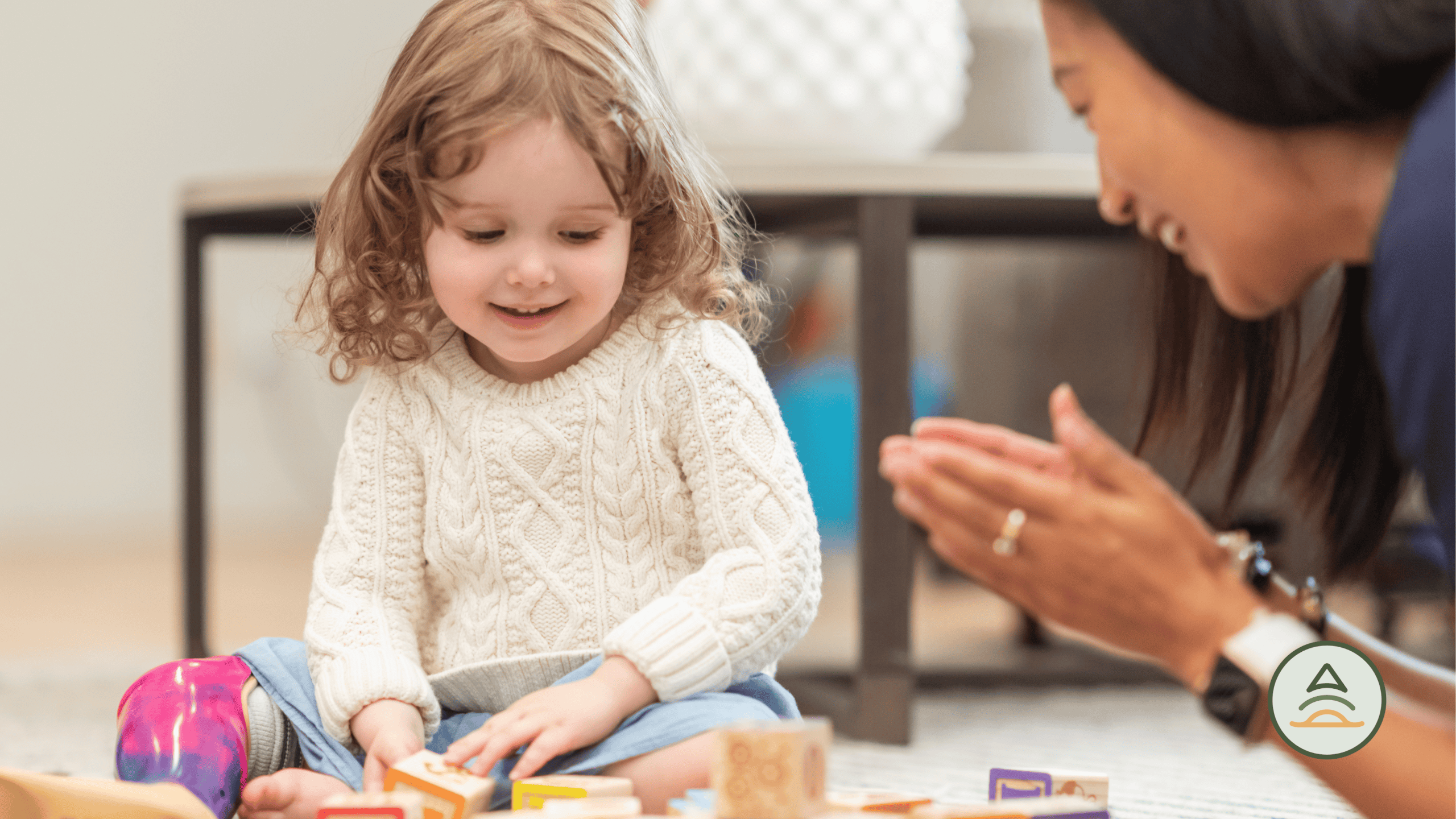 Child in a white sweater playing with toys near therapist.