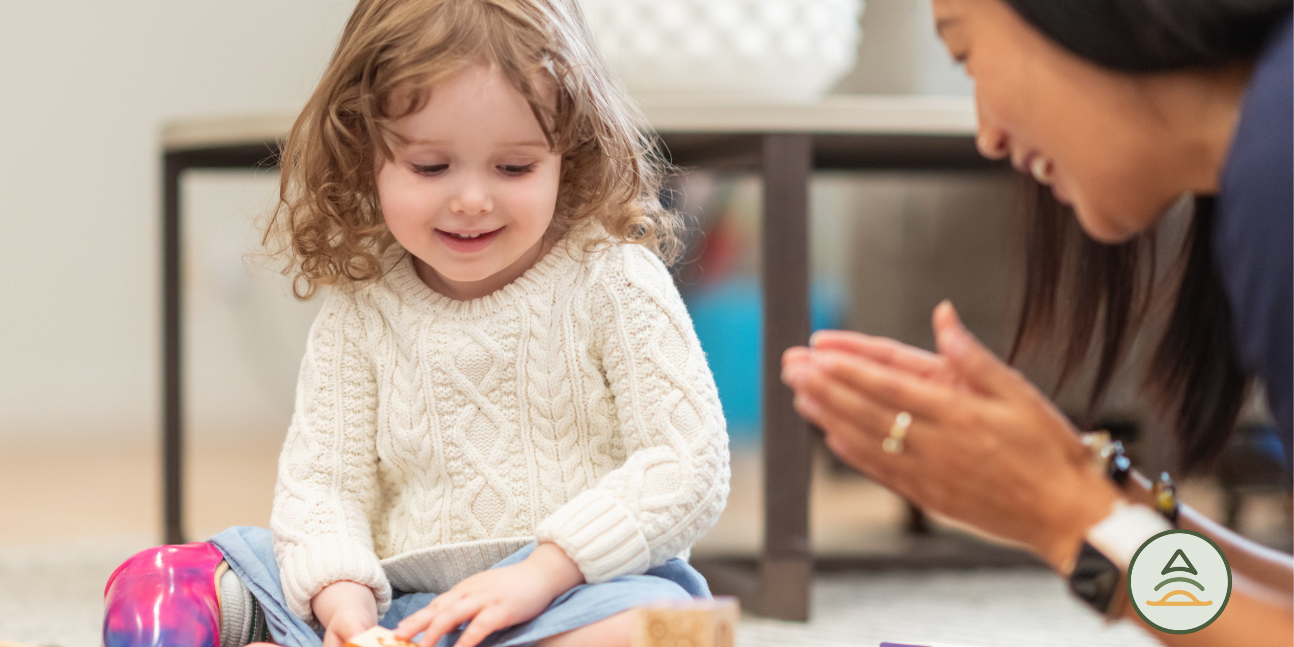 Child in a white sweater playing with toys near therapist.