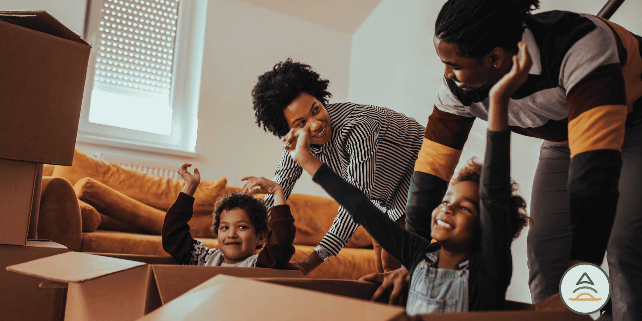 Man and woman with two children cheering and smiling in a living room with moving boxes.