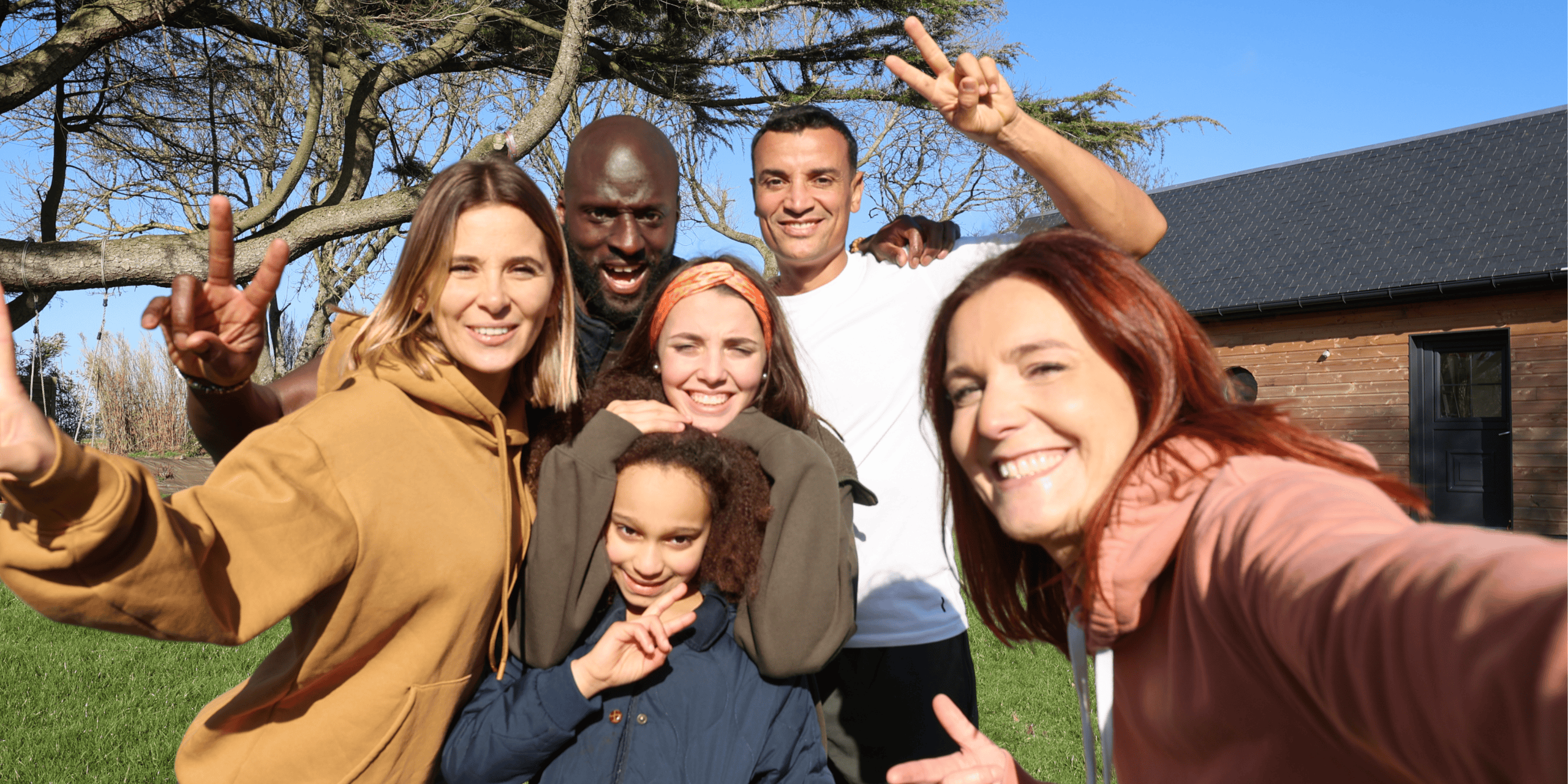 group of 3 women, 2 men and a child holding up peace signs standing together in a circle